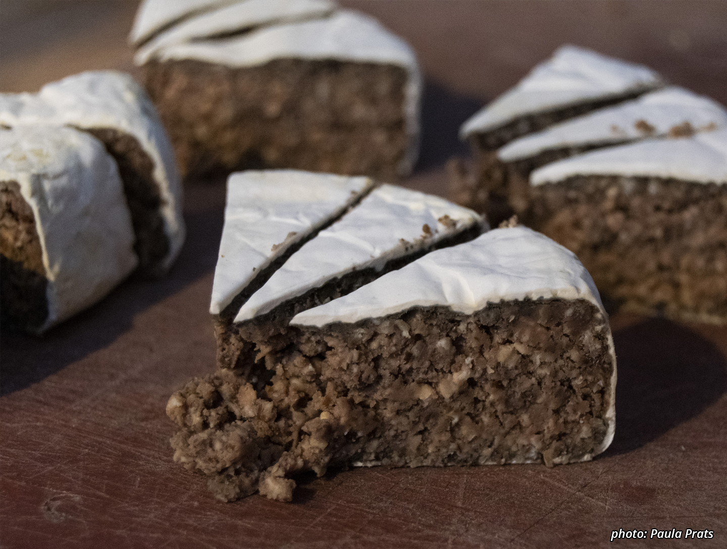 Picture of many triangles of lentil-oat camembert. The outside is a thin white rind, and the inside a brownish-black crumbly oat-lentil ferment.