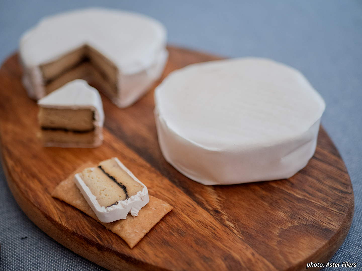 Picture of fermented cashew cheeses with crackers on a board. This shows fermented cashew mold-ripened with camembert and a layer of burnt leek running through it.