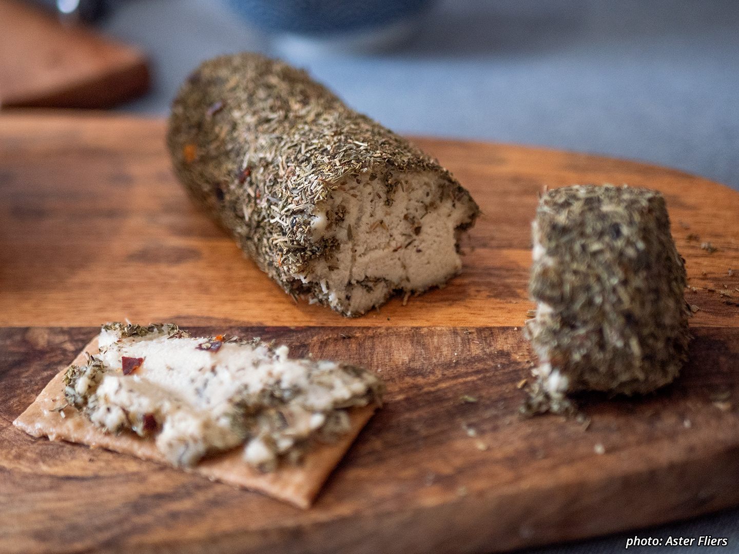 Picture of a creamy herbed roll of briefly fermented fresh cashew cheese, sliced through, with some of it spread on a cracker.